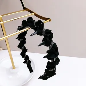 Detail of black rhinestone wave headband with punk spikes on a golden display stand