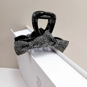 Elegant black bow hair claw clip with silver rhinestones on a minimalist background