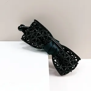 Détail de la pince banane nœud noir avec motif ajouré et strass brillants sur fond beige