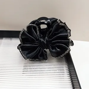 Détail d'une grande pince à cheveux en satin noir avec nœud et bordure en strass