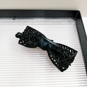 Détail d'une pince à cheveux banane nœud noir avec des strass brillants et design résille