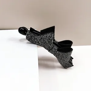 Détail d'une pince banane noire ornée de strass brillants sur une plateforme blanche