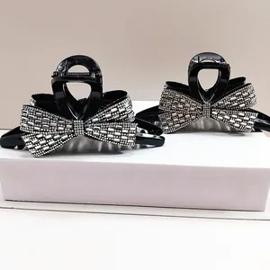 Detail of two black bow hair claws with sparkling rhinestones on white display blocks
