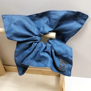 Dettaglio dello scrunchie a fiocco in denim blu con un emblema di coniglio in strass