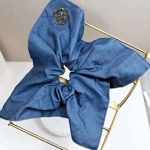 Detail of blue denim scrunchie featuring a black rhinestone camellia flower on a metal rack