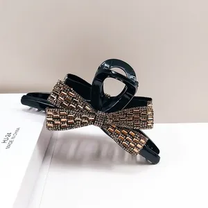 Macro detail of a crystal-encrusted bow hair claw clip with a black finish and gold rhinestones