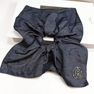 Detailed close-up of dark blue denim scrunchie featuring a luxury rhinestone camellia flower