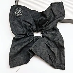 Detailed texture of charcoal denim scrunchie with sparkling rhinestone rose accent