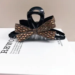 Close-up of a large black resin hair claw clip with crystal rhinestones in bow design