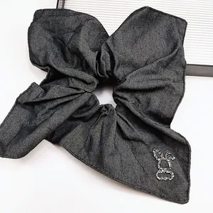 Dettaglio ravvicinato dello scrunchie in denim scuro con ornamento animale in strass
