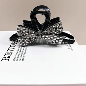 Detail of a black hair claw clip featuring a rhinestone bow design on a white box