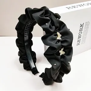 Détail d'un serre-tête en satin plissé noir orné de strass en forme de papillon brillant