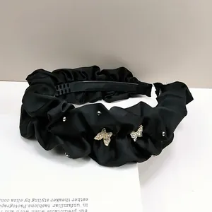 Détail d'un serre-tête en satin noir plissé orné de papillons en strass argentés brillants
