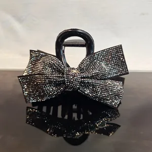 Elegant large black hair claw clip with silver rhinestone bow on a reflective surface