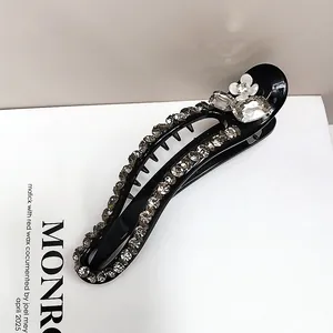 Detailed view of black resin hair claw clip with rhinestones and white floral accent