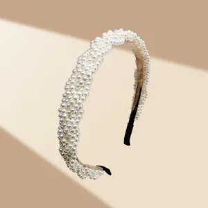 Detalle de diadema de perlas blancas hecha a mano con base de tela beige y puntas negras