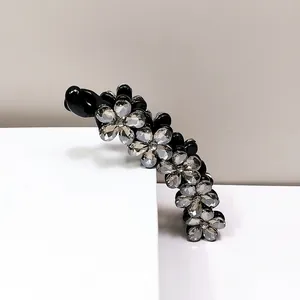 Dettaglio macro del fermaglio nero con fiori di cristallo su supporto bianco moderno