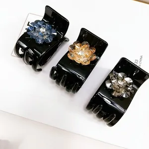 Close-up of three floral crystal hair claws in blue, champagne and grey on black base