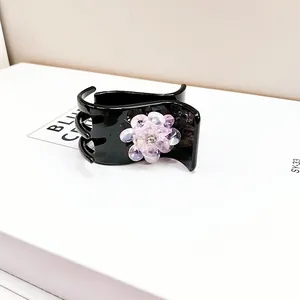 Detailed view of a black hair claw clip featuring a crystal flower and sparkling rhinestones