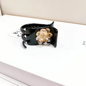Detail of a black hair claw clip featuring a champagne crystal flower with micro-engraving
