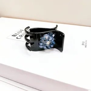 Detail of a black hair claw clip featuring a blue gradient crystal flower and rhinestones