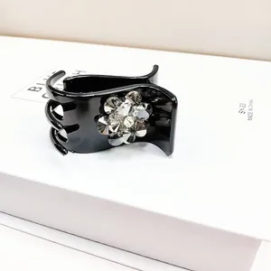 Close-up of black hair claw clip featuring a crystal flower and polished finish details