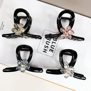 Close-up of four black hair claws featuring sparkling crystal flower designs in four colors