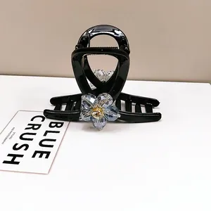 Detail of elegant black hair claw clip featuring a blue crystal flower with gold rhinestone