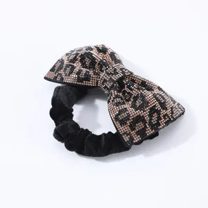 Dettaglio di elastico in velluto con fiocco decorato da strass neri e ambra leopardati
