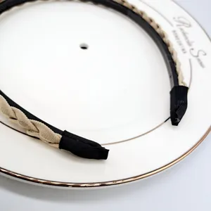 Close-up of beige braided detail on thin black headband headband on white ceramic plate