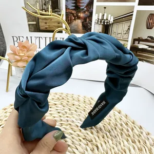 Close-up of teal satin pleated headband featuring a handmade label and silky texture