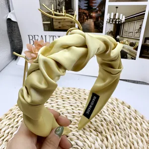 Detailed close-up of champagne satin pleated headband with handmade label and knot design