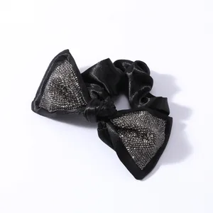 Dettaglio di scrunchie in seta nera con fiocco in strass scintillanti e nodo centrale