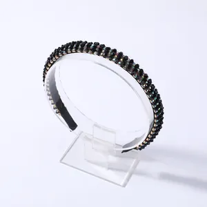 Detalle de diadema negra fina con pedrería iridiscente multicolor sobre un soporte transparente