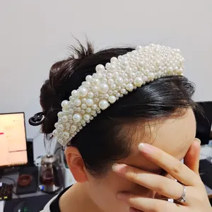 Detailed close-up of a wide padded headband featuring elegant faux pearls on white fabric