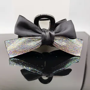 Close-up of a large black hair claw clip with satin bow and colorful rhinestones