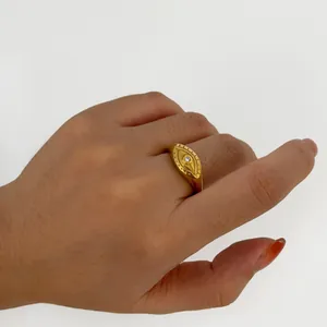 Gold evil eye signet ring with inlaid zircon gemstone shown on hand in a white background