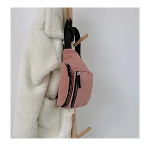 Pink corduroy crossbody bag with double zippers hanging on a wooden rack