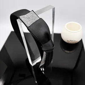 Detail of black satin headband featuring a crystal-encrusted rectangular patch and side beading