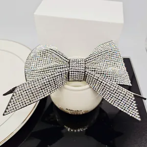 Detailed close-up of a large bow hair clip with luxury rhinestones on a reflective surface