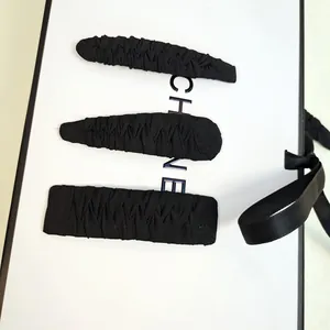 Set of three black fabric hair clips in geometric shapes on a white gift box