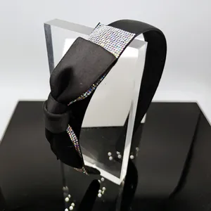 Dettaglio ravvicinato del cerchietto in raso nero con un grande fiocco di strass colorati