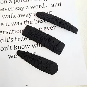 Detailed view of three black fabric textured hair clips set on a minimalist background