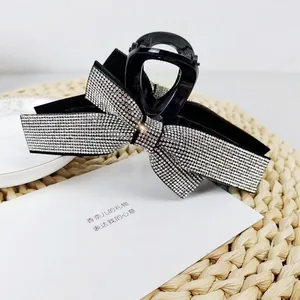 Detail of elegant black hair claw clip featuring a large bow set with shimmering rhinestones