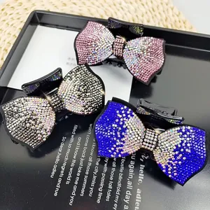 Three rhinestone bow hair claws in pink, silver and blue displayed on a black tray