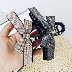 Detail view of two rhinestone bow claw clips in champagne gold and deep grey colors