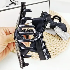 Détail d'une grande pince à cheveux noire avec un nœud en soie et des strass brillants