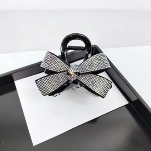 Détail d'une pince à cheveux en résine noire avec nœud en strass étincelants sur un plateau