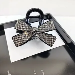 Détail d'une pince à cheveux noire ornée d'un nœud en strass et d'un ressort en métal