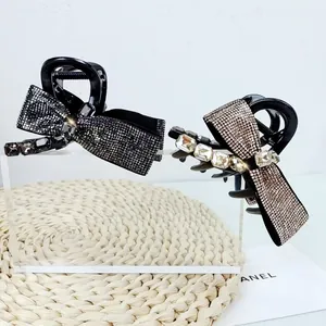 Detail showing elegant bow hair claws with sparkling rhinestones on an acrylic stand